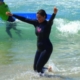 woman in a wetsuit smiling and raising her hands after learning how to surf