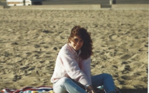 Adolescent Karen Pery smiling at the camera while sitting on a beach
