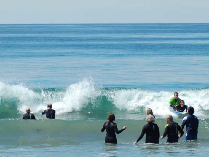 People in wetsuits wading into the ocean